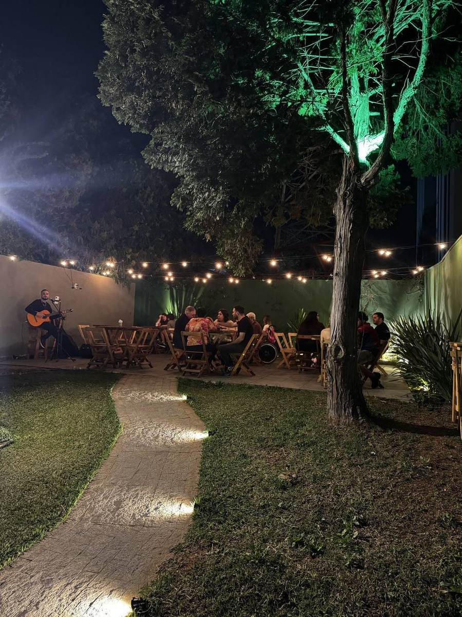 Quintal do Arvrão Burger cheio à noite, com mesas sob o varal de luzes